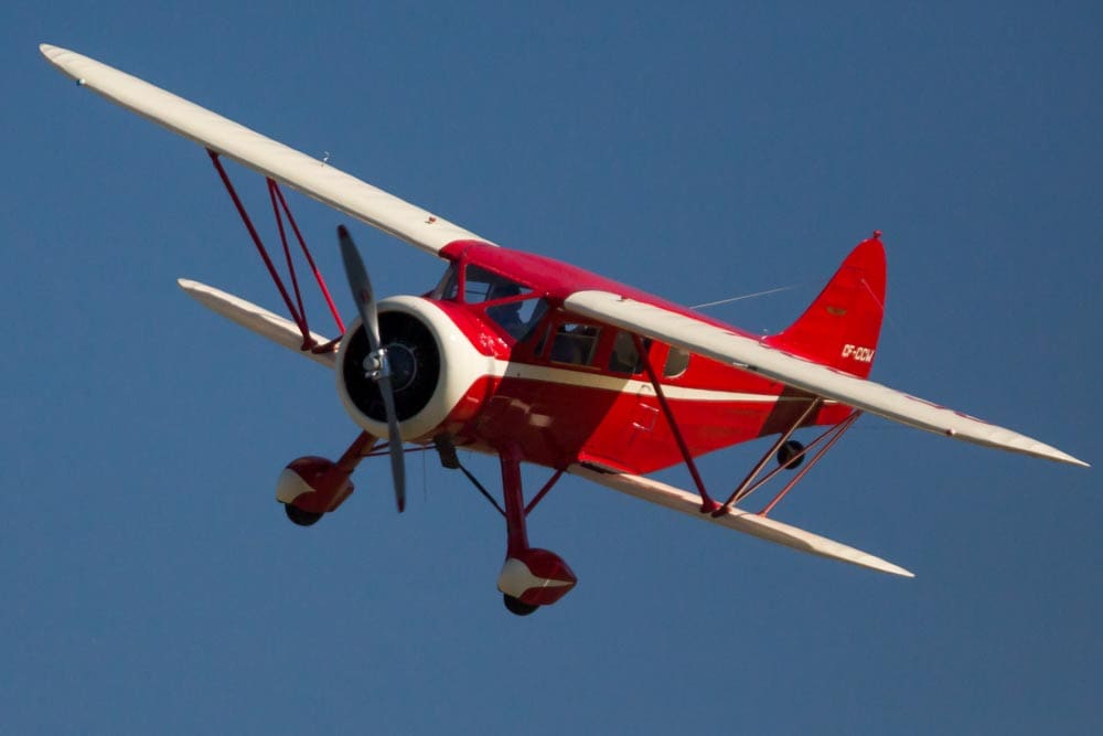 Red and white biplane banking in flight at an airshow at Paine Field, Washington, propeller frozen mid-spin against a clear blue sky