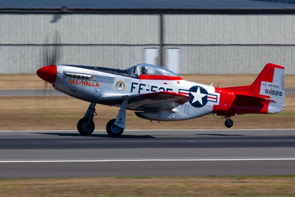 Vintage P-51 Mustang fighter plane landing at an airshow at Paine Field, Washington, propeller blurred into a translucent disc
