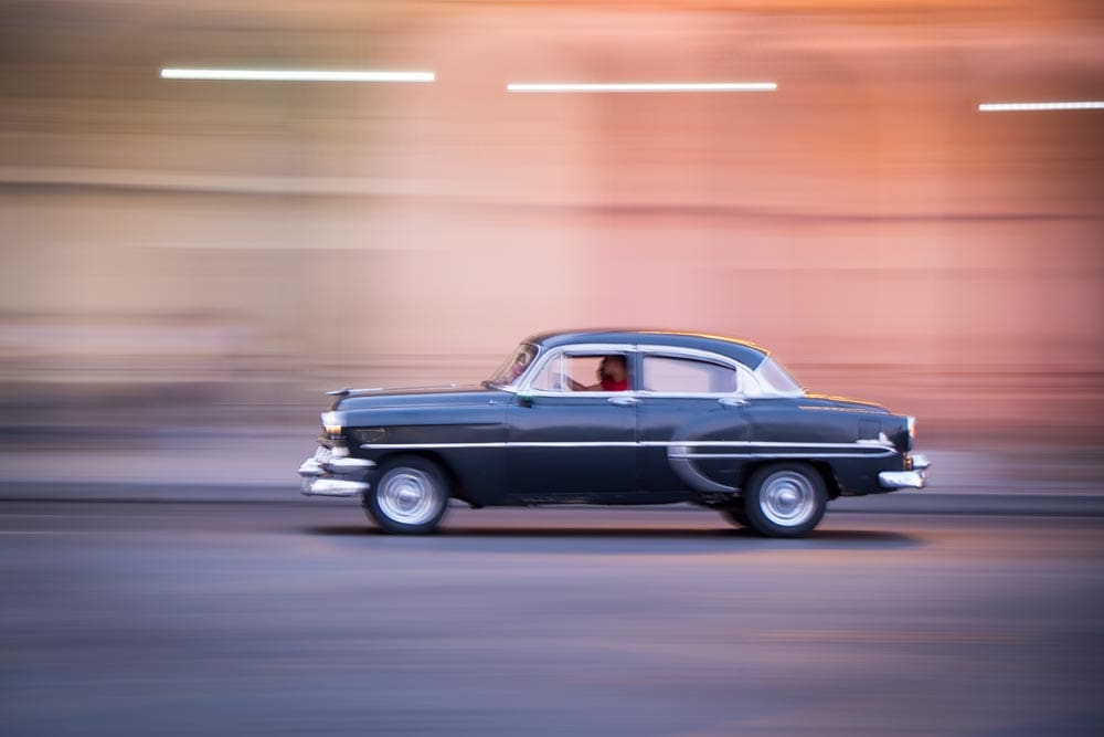 Dark vintage car speeding through Havana, Cuba, background lights and buildings rendered as long horizontal streaks from panning