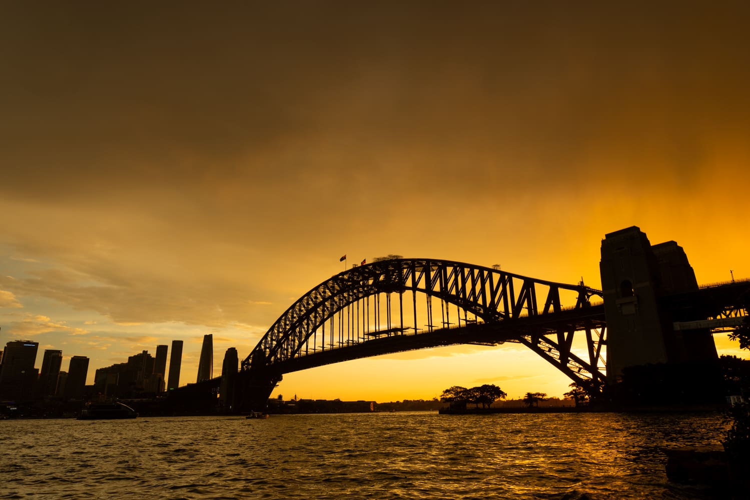 Sydney Harbour Bridge silhouetted against a glowing golden sunset, with the city skyline at left