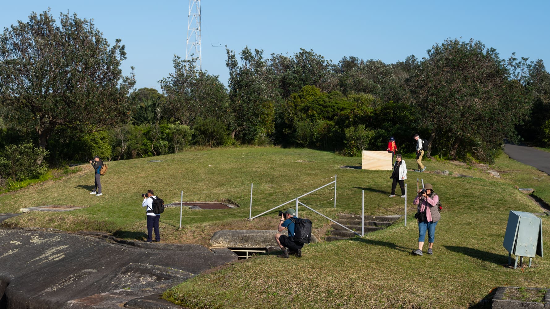 Tour photographers spread out across a grassy former military site, taking pictures on a sunny morning