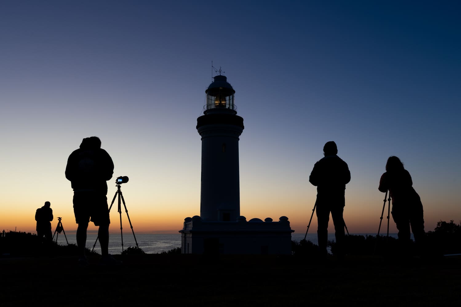 Photographers with tripods silhouetted at dawn beside Norah Head Lighthouse on the Central Coast of New South Wales
